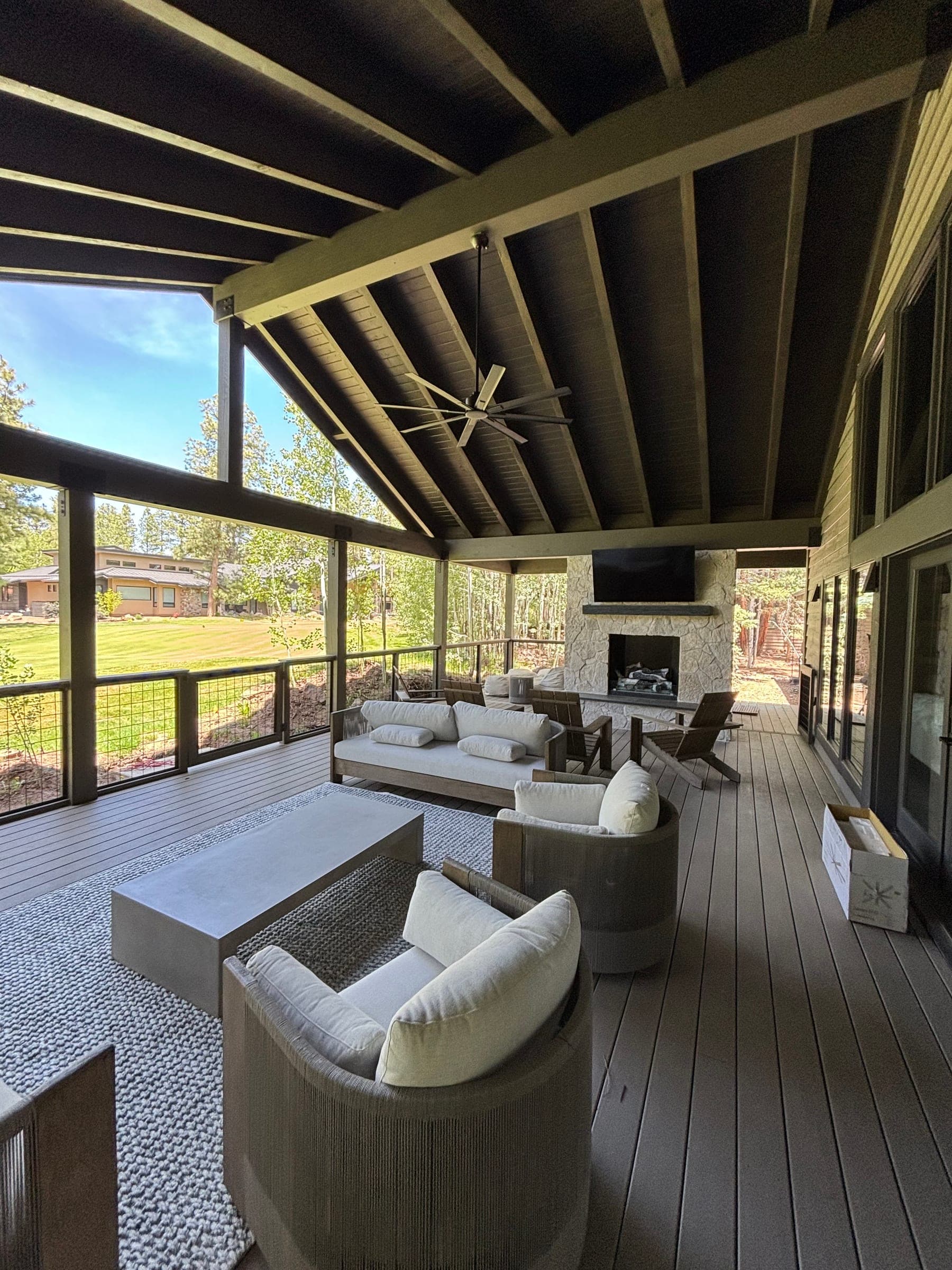 Furnished covered patio with outdoor seating, a stone fireplace with a mounted television and open views through aspens