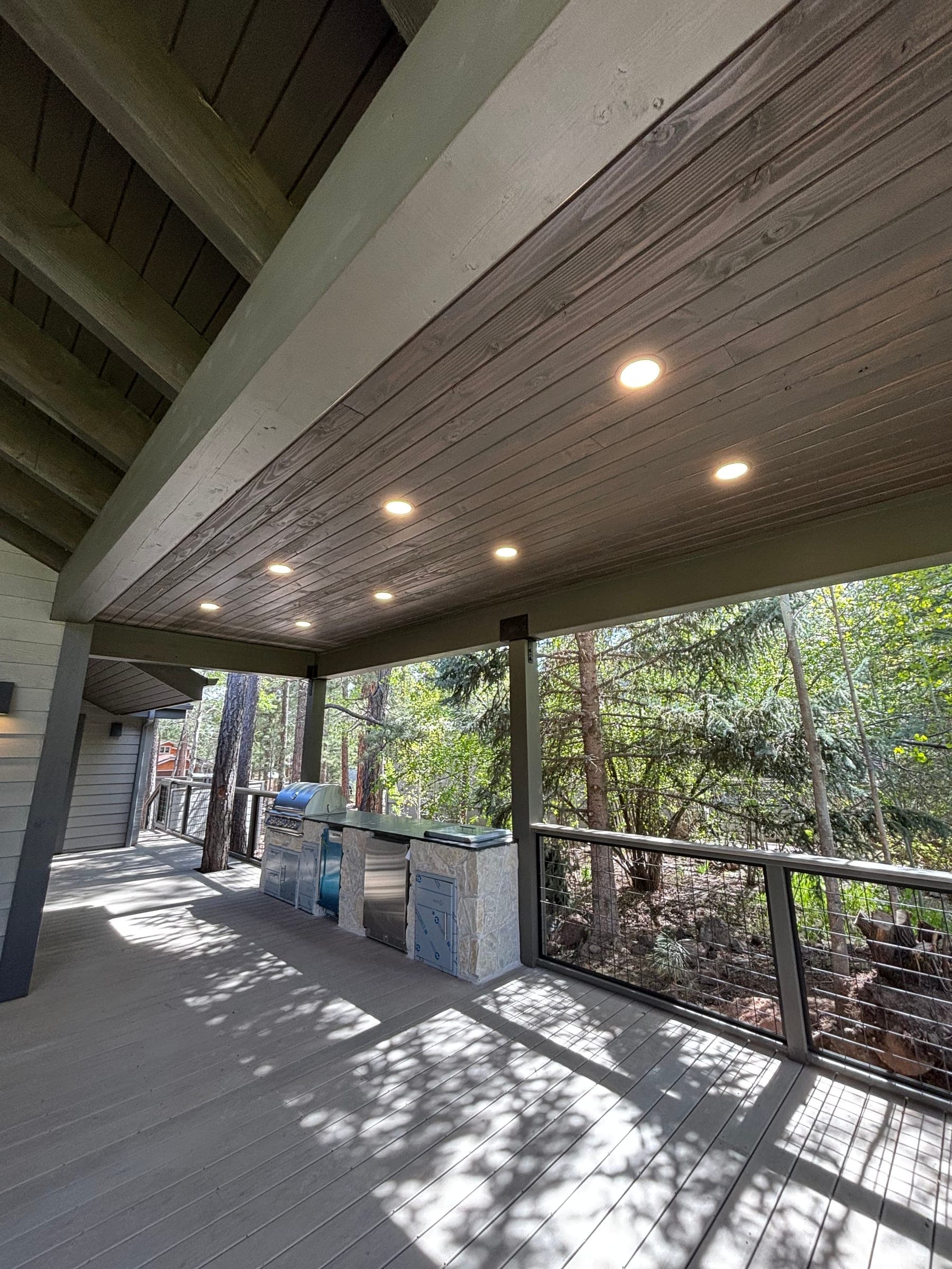 Covered deck with tongue-and-groove soffit, recessed lighting and a stone outdoor kitchen counter, appliances still wrapped in protective film
