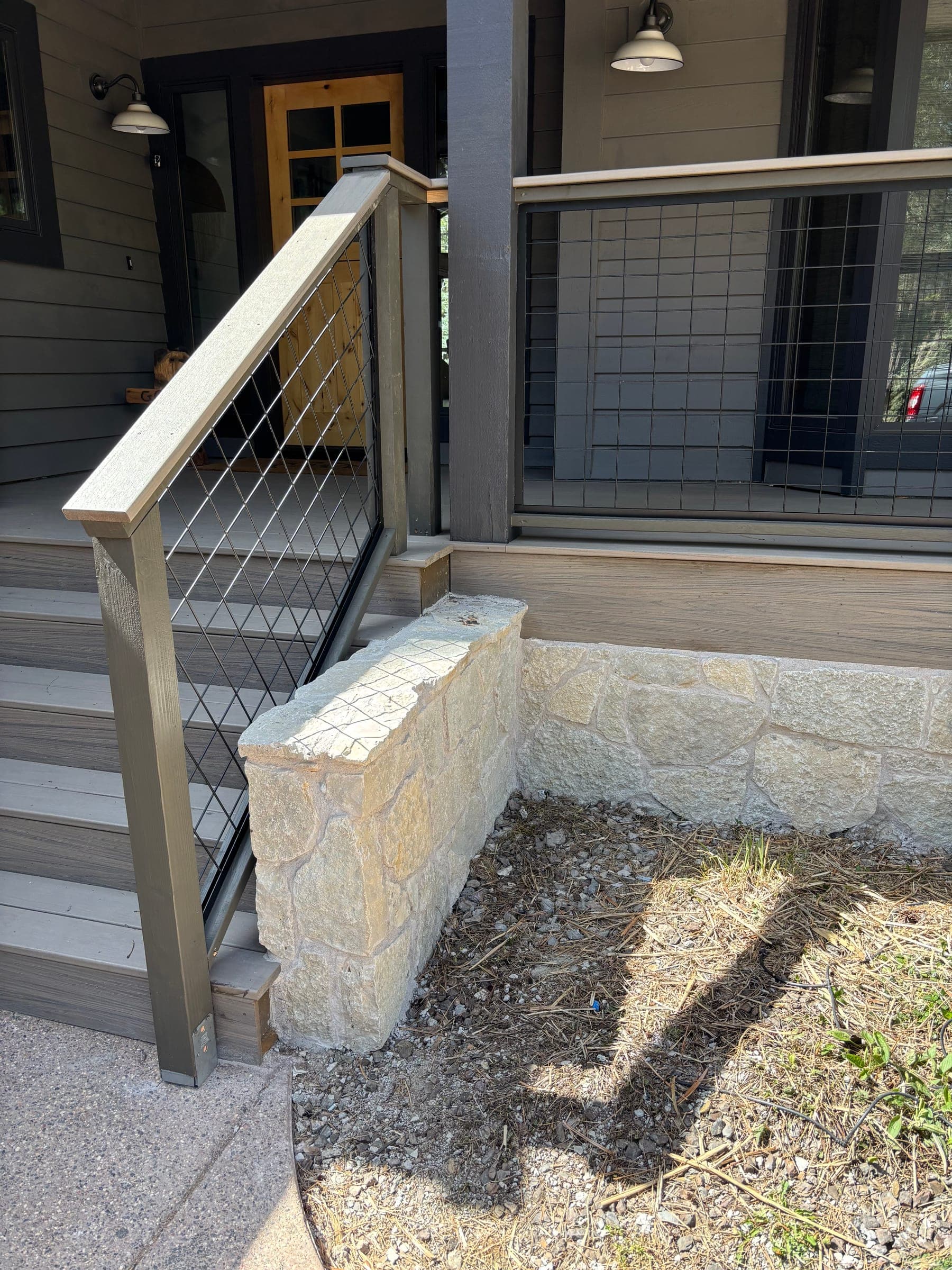 Wire-mesh panel railing meeting a stone wall and a solid stone bench slab set on gravel