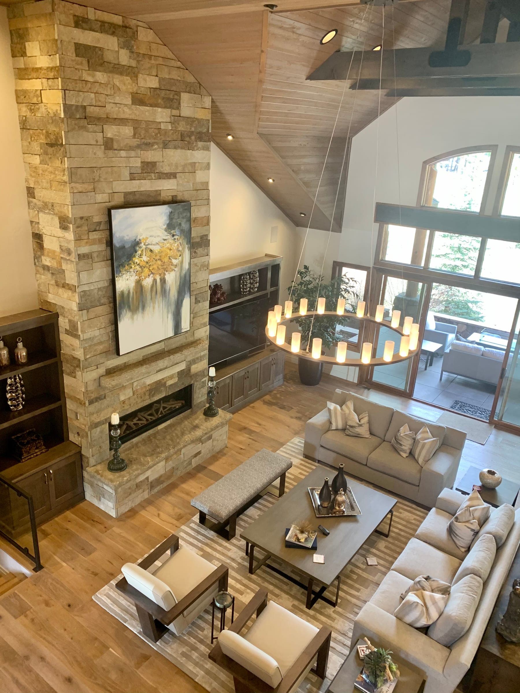 Great room seen from a loft: full-height stacked stone fireplace, vaulted tongue-and-groove ceiling and a ring chandelier