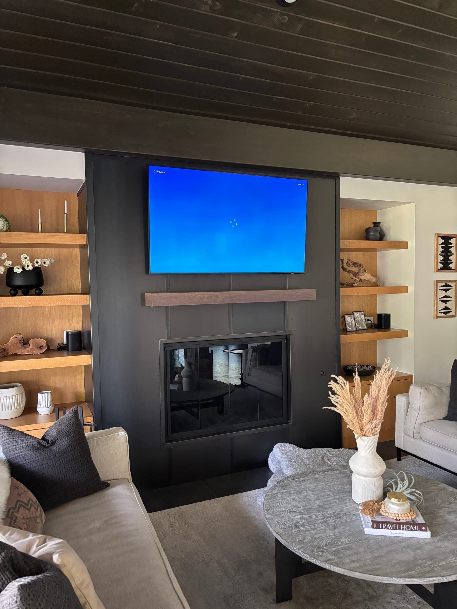 Living room with a dark panelled fireplace surround, wood mantel, white oak floating shelves and a dark tongue-and-groove ceiling