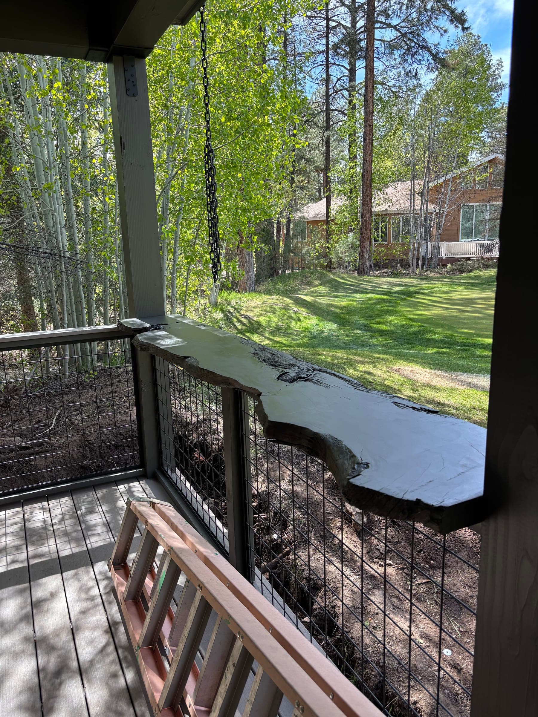 Lower covered deck with a live-edge slab bar top and wire-mesh railing, aspens beyond