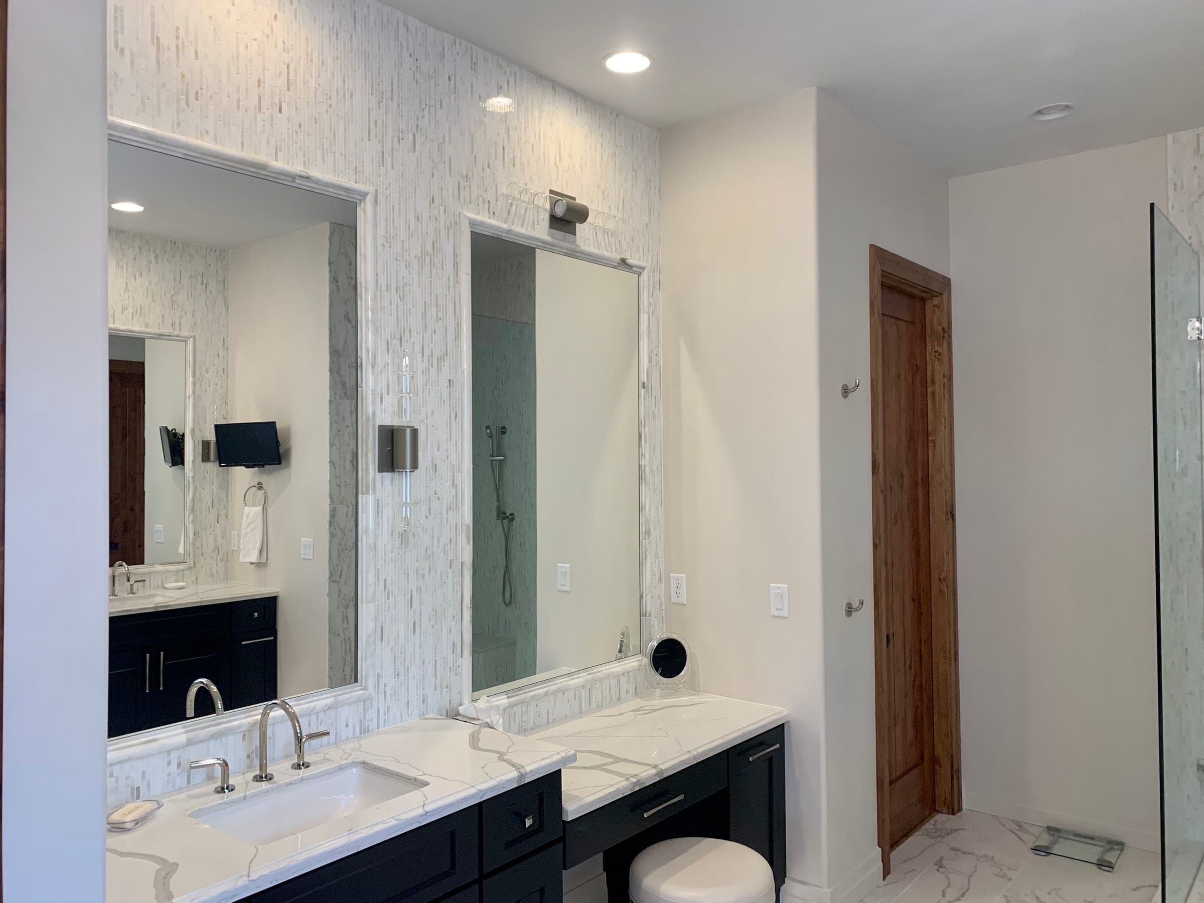 Master bathroom with twin dark vanities, stone counters, a linear mosaic tile feature wall and framed mirrors