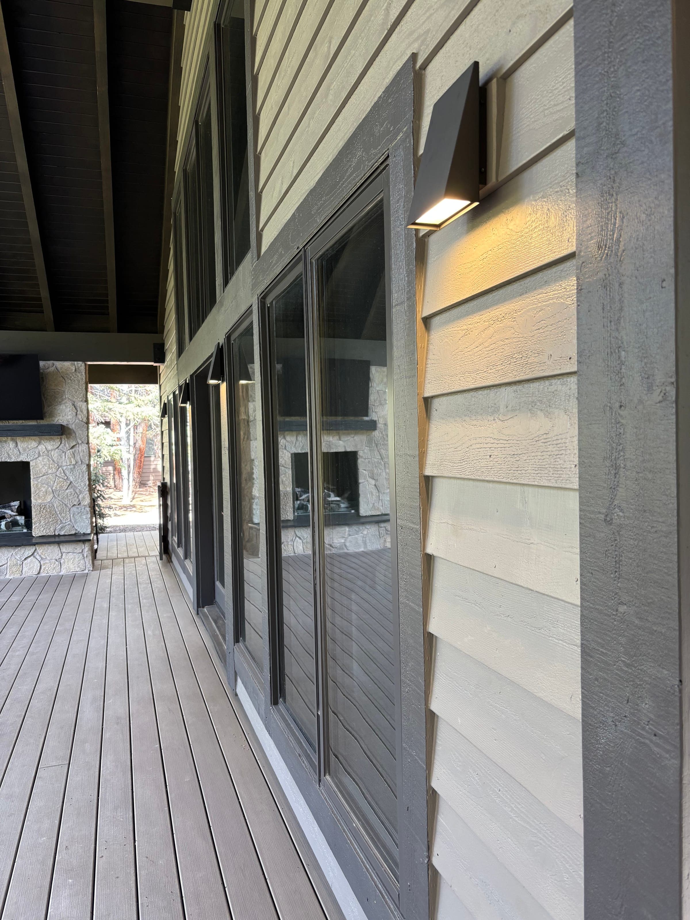Covered porch with lap siding, sliding glass doors and downlit sconces, looking toward a stone-clad outdoor fireplace